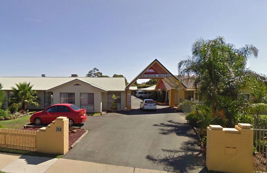 a view of a driveway leading to a yellow building with trees in the background at Echuca Motel
