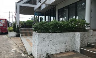 a white house with a gray roof and bushes growing near the entrance , and a stone wall surrounding the entrance at Triple Resort