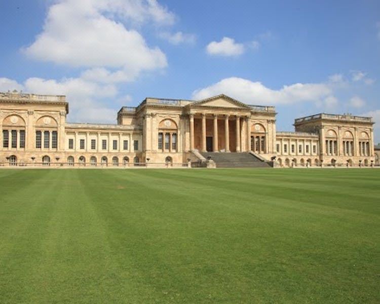 a large , historic building with columns and a green lawn in front of it , under a blue sky with clouds at Villiers Hotel