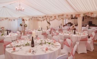 a wedding reception with white tablecloths , pink napkins , and wine glasses on tables set for dinner at St Quintin Arms