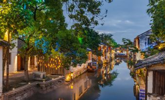 At night, a canal in the city is illuminated by lights, with houses lining both sides of the water at Zhouzhuang Latte Play Stone Mulan Hotel