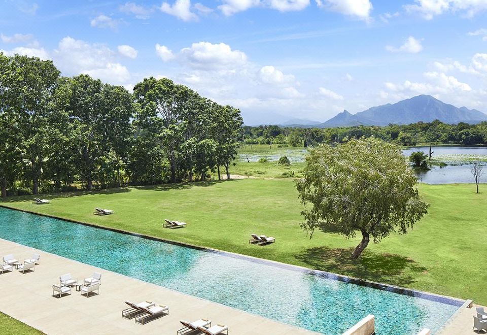 a large pool with lounge chairs and a view of a lush green field and mountains in the background at Jetwing Lake