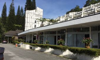 a modern building with a white exterior and large windows is surrounded by greenery and flower pots at Shahzan Inn Fraser's Hill