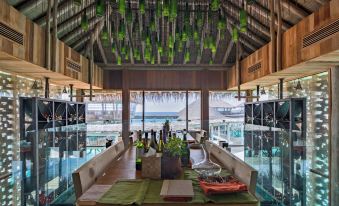 a wooden dining room with a long wooden table surrounded by chairs , and a glass ceiling hanging from the ceiling at Six Senses Laamu