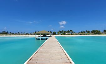 a wooden pier extending into the turquoise water , with a small hut on an island in the distance at South Palm Resort Maldives