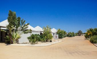 a row of white tents in a sandy area with trees and a clear blue sky at Exmouth Escape Resort