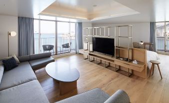 a modern living room with wooden floors , large windows offering views of the ocean , and a flat - screen tv at Hotel Anteroom Naha