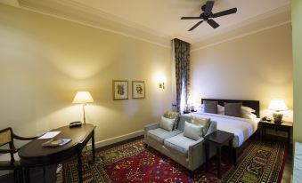 a cozy bedroom with a bed , a couch , and a tv . the room is well - lit , and a ceiling fan above the bed at Galle Face Hotel