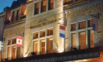 a large building with multiple flags flying in front of it , creating a festive atmosphere at Hotel Manoir Victoria