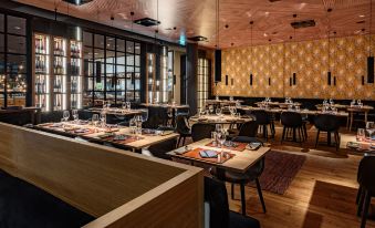 A restaurant with tables and chairs arranged in the center, facing each other on both sides at Clarion Hotel Aviapolis