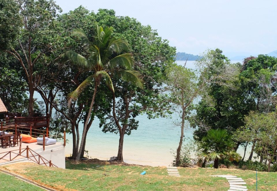 a beach scene with a grassy area , palm trees , and a view of the ocean at Phayamas Private Beach Resort and Island Brew - Adults Only