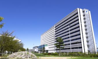 a modern building with a white facade and large windows , situated in a sunny environment with trees and grass at Centrair Hotel