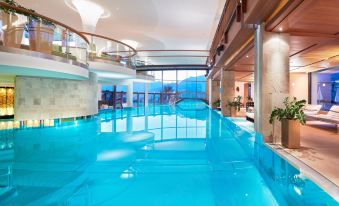 an indoor swimming pool with blue water , surrounded by a glass wall and a marble floor at Schlosshotel Fiss
