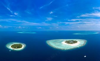 two small islands in the ocean , surrounded by blue water and white sandy beaches , with a cloudy sky above at Banyan Tree Vabbinfaru