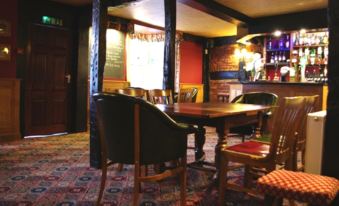 a cozy pub with wooden furniture , including a table and chairs , as well as a bar area with various bottles and glasses at The Corners Inn
