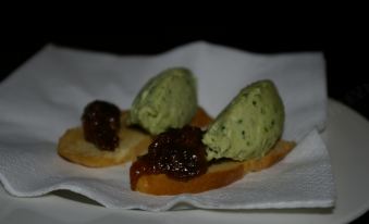a white plate with three small , green ice cream cones topped with various sauces , placed on a bed of crackers at The Foxham