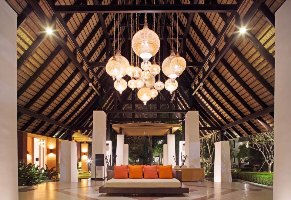 a spacious hotel lobby with an open floor plan , wooden beams , and large hanging lights at Mida Resort Kanchanaburi