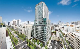 a tall , modern building in the middle of a busy city street , surrounded by other buildings and cars at The Royal Park Hotel Iconic Osaka Midosuji