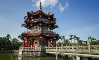 a traditional chinese pagoda - style building situated on a stone bridge over a body of water , surrounded by lush greenery at Han She Business Hotel