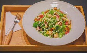 A plate with salad and a spoon is placed next to another dish containing meat at Desti Youth Park Hostel (Xi'an Bell Tower)