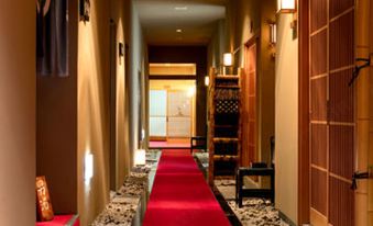 a long hallway with a red carpet and wooden doors , featuring a stone bench at the end at Ryokan Warabino