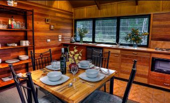 a dining table is set with white plates , wine glasses , and a bottle of wine in a kitchen at Girraween Environmental Lodge