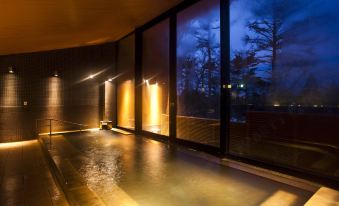 a modern , minimalist indoor swimming pool with large windows and wooden ceiling , illuminated by warm lights at Karuizawa Prince Hotel East