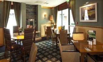 a cozy restaurant with wooden tables and chairs , large windows , and green walls , providing a warm and inviting atmosphere at Oswestry