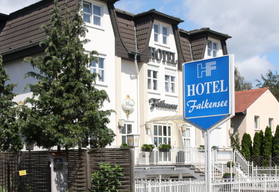 a large hotel building with a blue sign in front of it , surrounded by trees at Falkensee