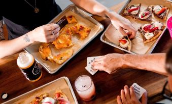 a group of people gathered around a dining table , enjoying a meal of pizza and drinks at Moxy Edinburgh Airport