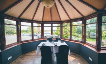 a dining room with a table set for two , surrounded by windows that provide a view of the outdoors at The Grange Hotel Brent Knoll