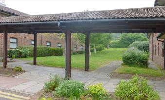 a covered walkway with a brown tiled roof , surrounded by greenery and a brick building in the background at Premier Inn Dover East
