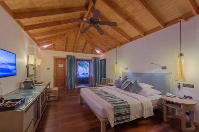 a bedroom with a large bed , wooden floors , and a ceiling fan with a curtain at Vilamendhoo Island Resort & Spa