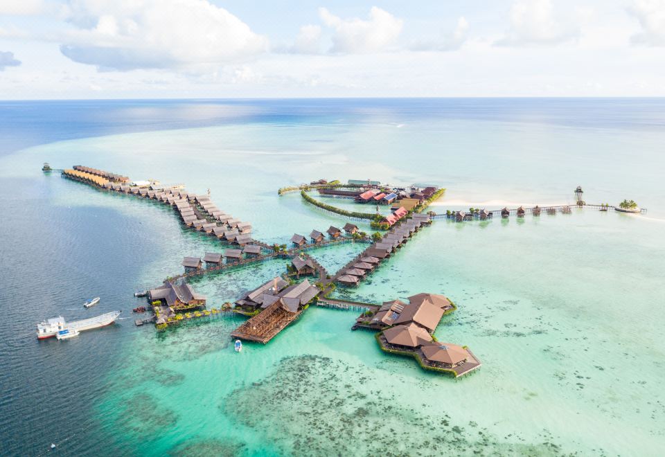 An aerial view displays a resort and the water surrounding it, featuring a sizable wooden pier at Sipadan Kapalai Dive Resort