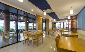 a modern restaurant with wooden tables and chairs , large windows , and a blue ceiling , under the supervision of a large glass door at Siva Royal Hotel