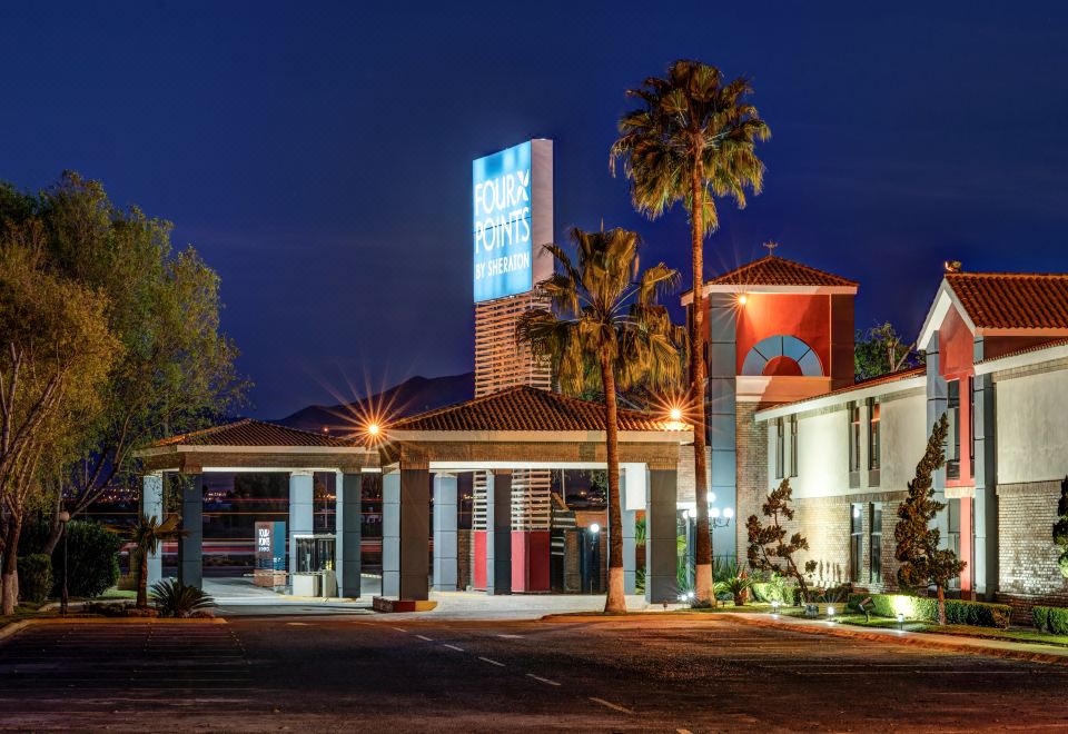 "a nighttime view of a motel with palm trees and a large sign that says "" heritage inn "" in blue" at Four Points by Sheraton Saltillo