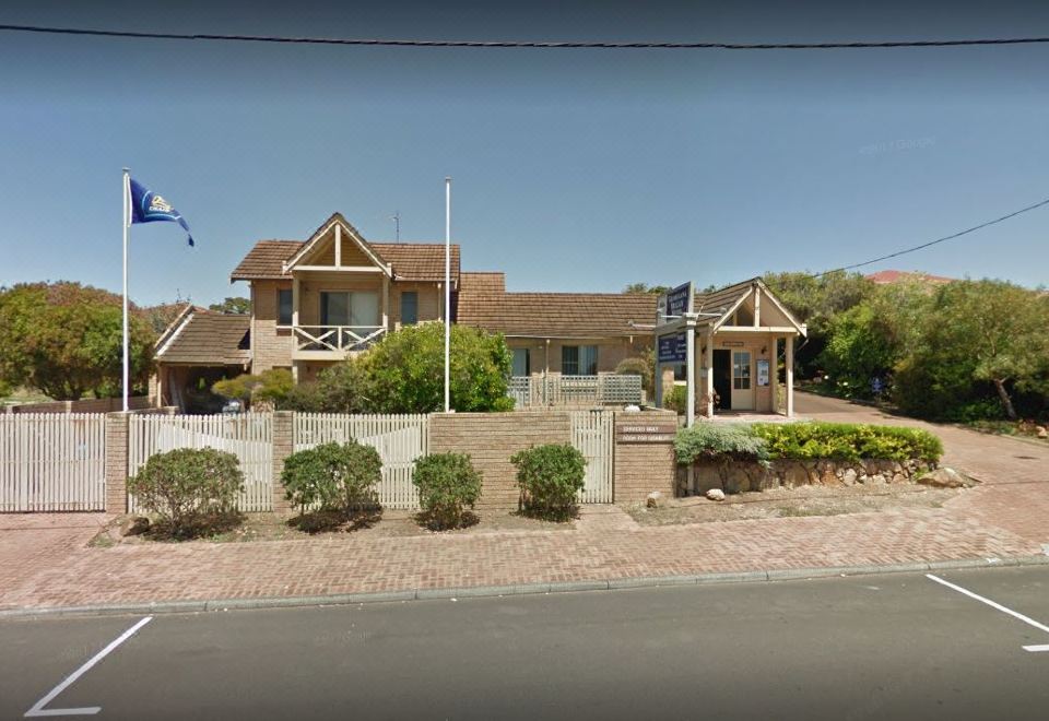 a large house with a wooden fence and flags is shown in the image , surrounded by bushes at Augusta's Georgiana Molloy Motel