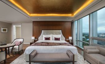a luxurious bedroom with a large bed , wooden headboard , and floor - to - ceiling windows offering views of the city at Lotte Hotel Yangon