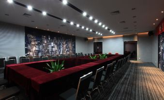 a large conference room with a long table , chairs , and a screen displaying an image of a city skyline at M Hotels