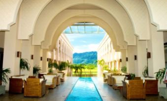 a large indoor pool surrounded by lounge chairs and a palm tree , with mountains in the background at The Pade Dive Resort