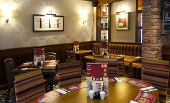 a restaurant with wooden tables , chairs , and booths , as well as menus on the tables at Premier Inn Maidstone (West Malling) hotel
