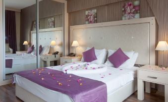 a luxurious hotel room with a large bed , white sheets , and purple linens , along with rose petals scattered on the bed at Manolya Hotel