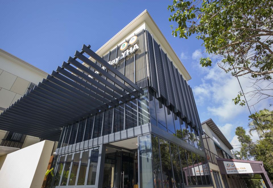 a modern building with a glass facade and metal support beams , under a clear blue sky at YHA Byron Bay