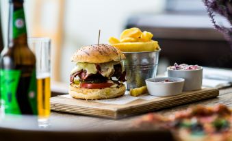 a wooden dining table with a plate of food , including a burger , fries , and a glass of beer at The Oakhill Inn
