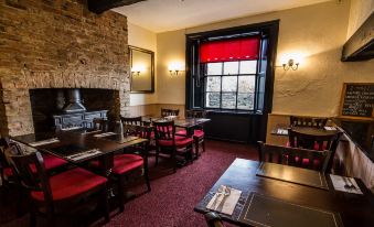 a cozy dining room with wooden tables and chairs , red curtains , and a fireplace near the window at The Oddfellows Arms