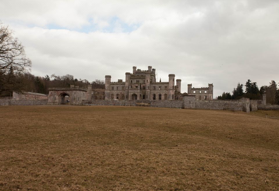 a large stone castle is surrounded by a grassy field and trees , with a cloudy sky overhead at The Punchbowl Inn