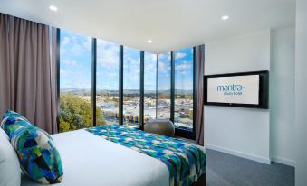 a modern bedroom with large windows offering a view of the city , featuring a comfortable bed and a blue comforter at Mantra Albury Hotel
