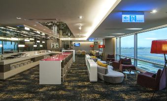 a modern airport lounge with multiple couches , chairs , and tables , as well as an inviting bar area at Novotel Taipei Taoyuan International Airport