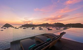 a wooden deck overlooking a body of water at sunset , with a row of sailboats in the distance at Meruorah Komodo Labuan Bajo