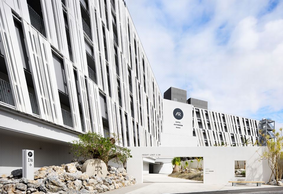 a modern building with a large sign on the side , surrounded by trees and rocks at Hotel Anteroom Naha